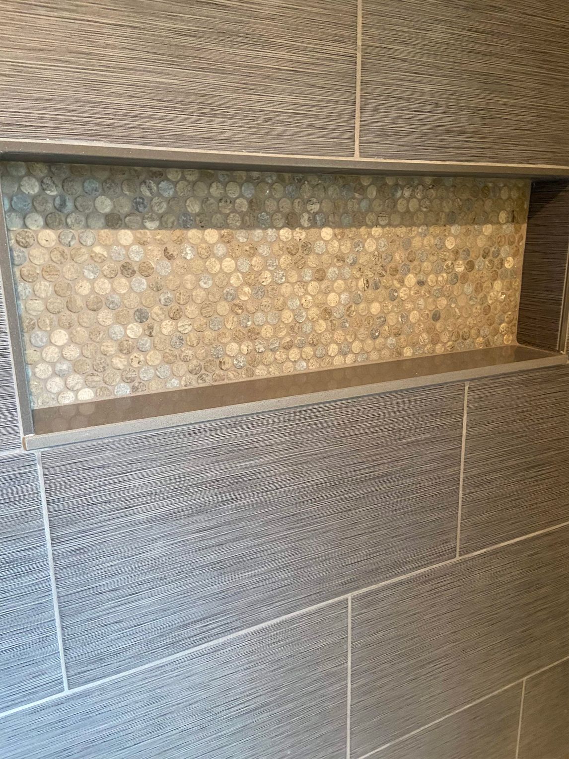 Textured tiled wall niche with small pebble mosaic accents and gray stone tiles