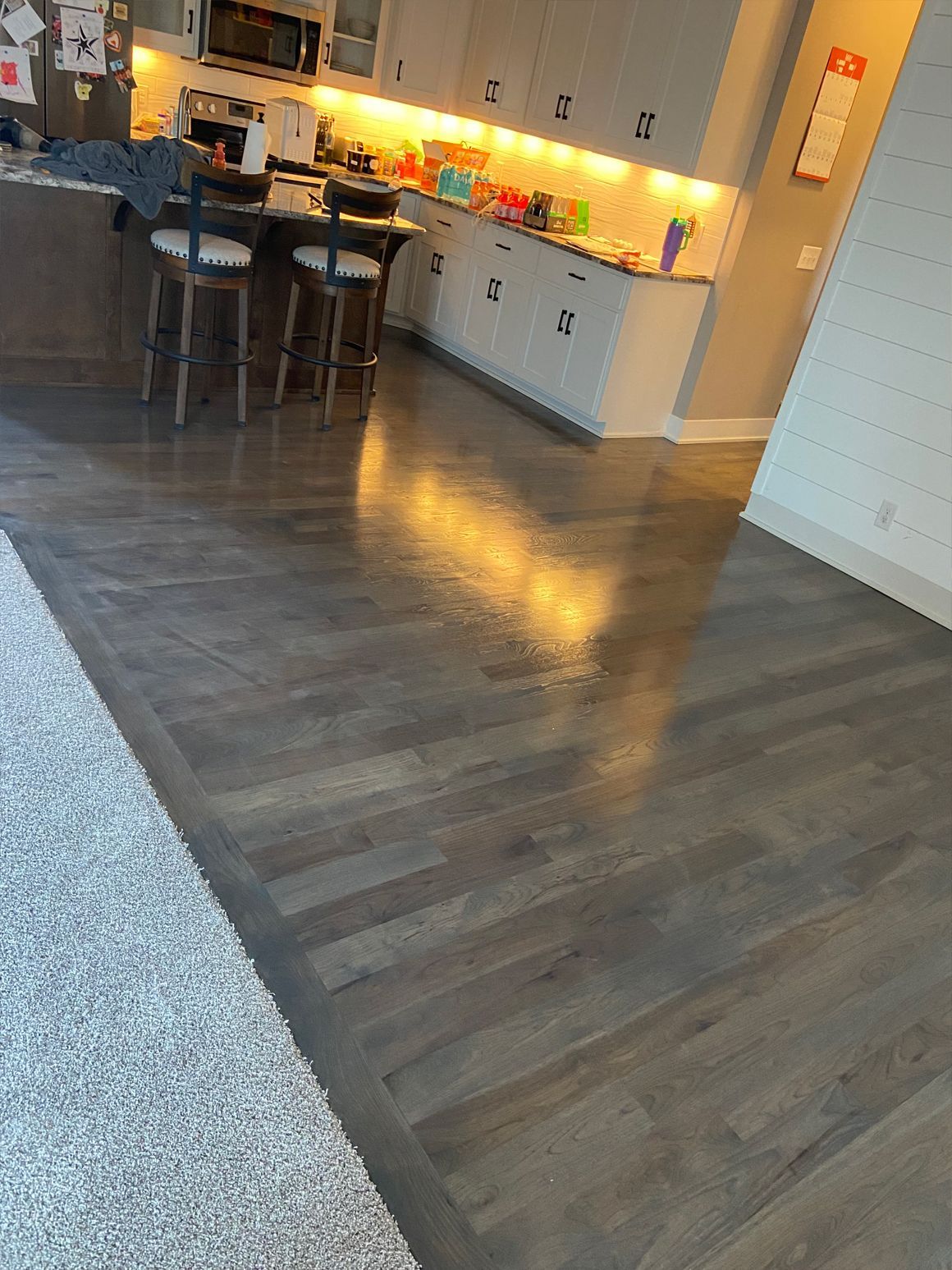 Modern kitchen with dark wood floor, white cabinets, island, and warm under-cabinet lighting