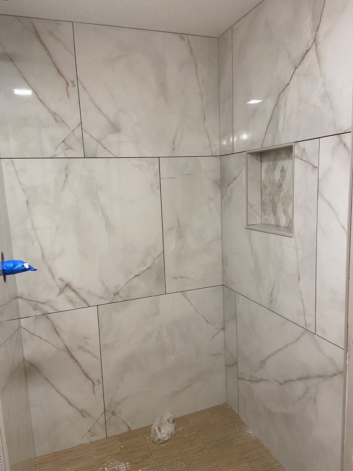 Tiled shower stall with marble-look walls, beige floor, and a small recessed shelf