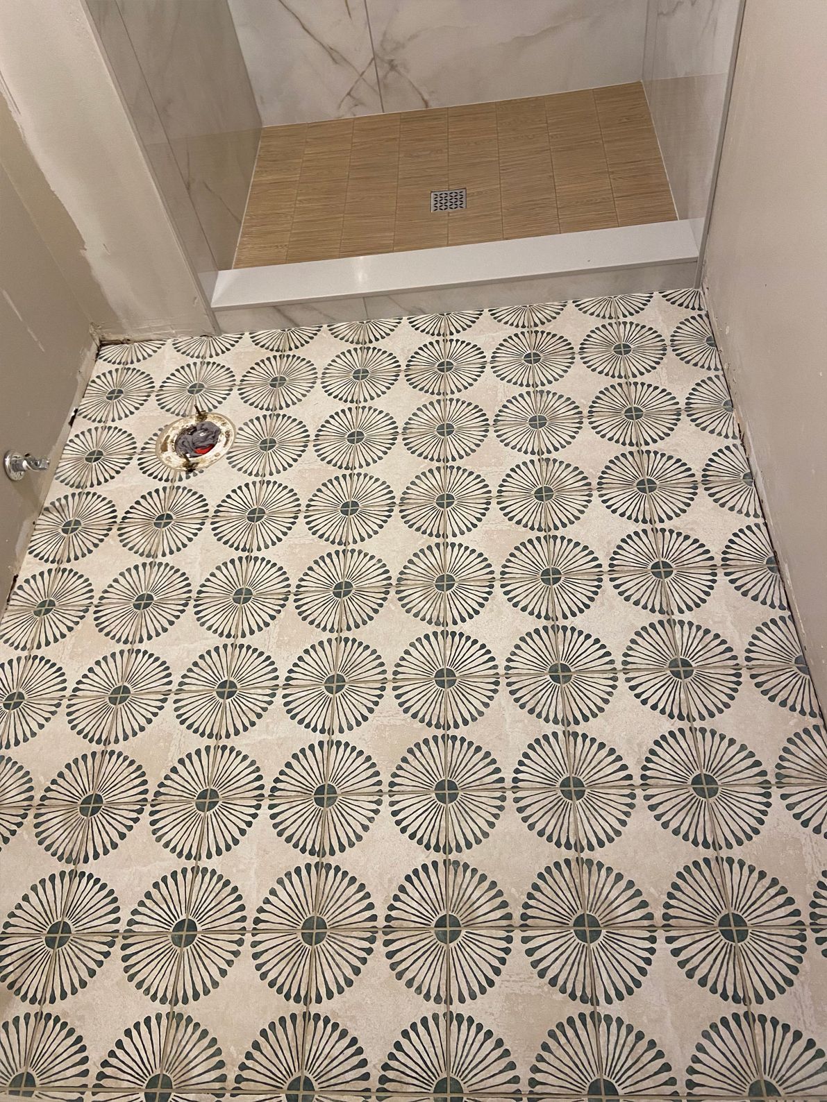 Patterned tile bathroom floor with a small recessed shower area and drain at the top.