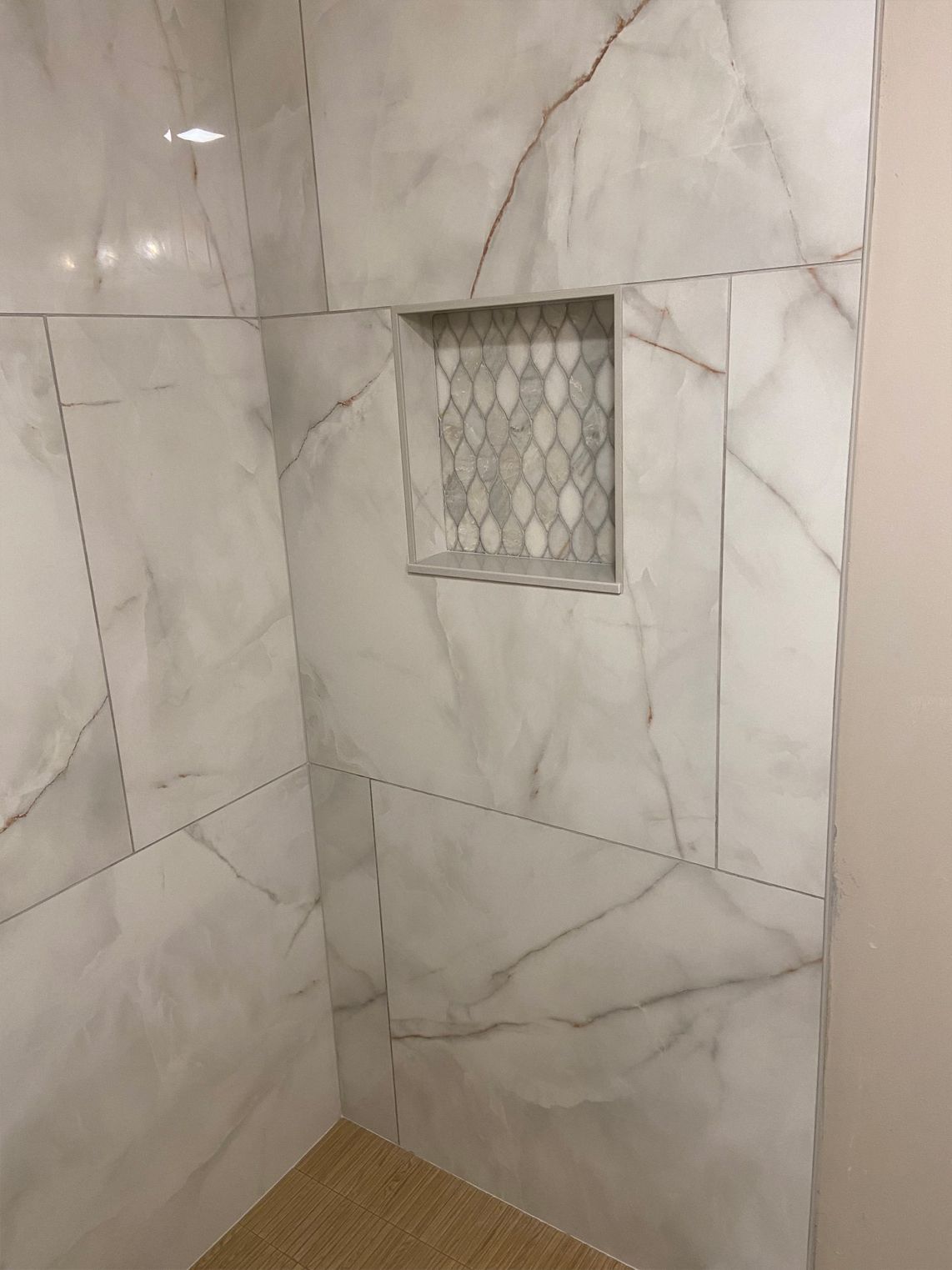Tiled shower wall with recessed niche and small mosaic accent, beige and white marble pattern