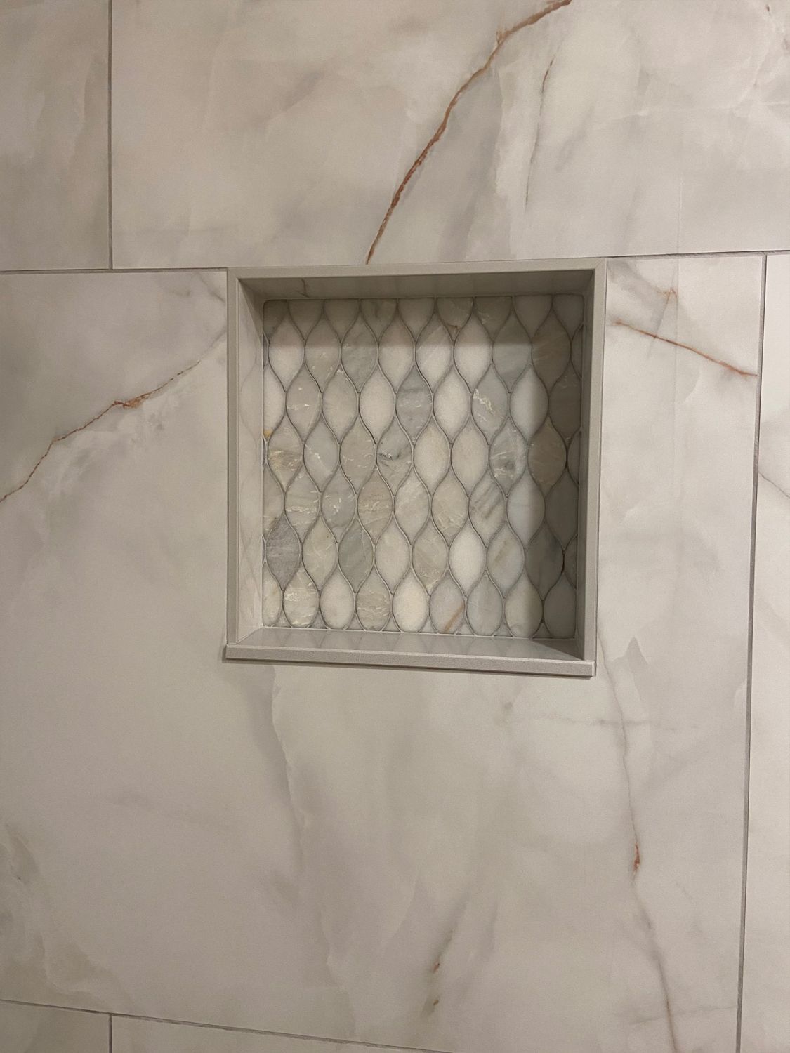 Marble-tile shower wall with a recessed niche and patterned mosaic insert