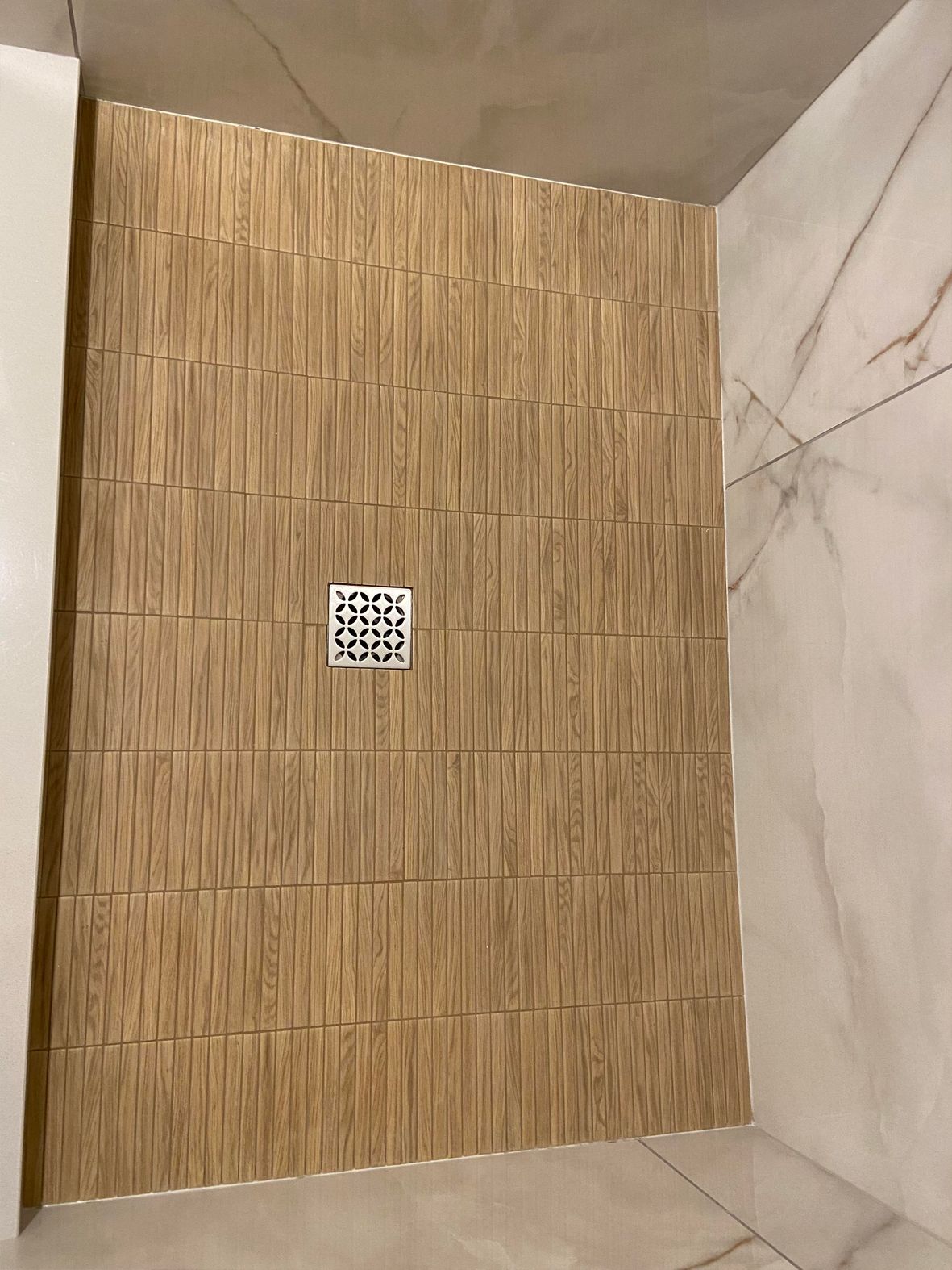 Tiled shower wall with tan wood-look tiles and a small square mosaic accent in the center