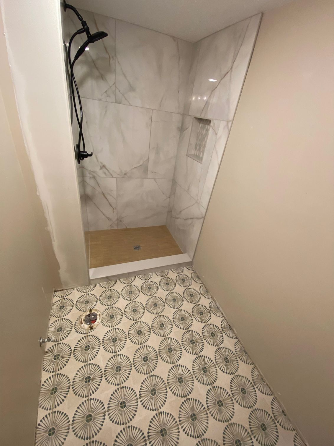 Small bathroom with patterned tile floor and marble shower stall, viewed through a doorway.