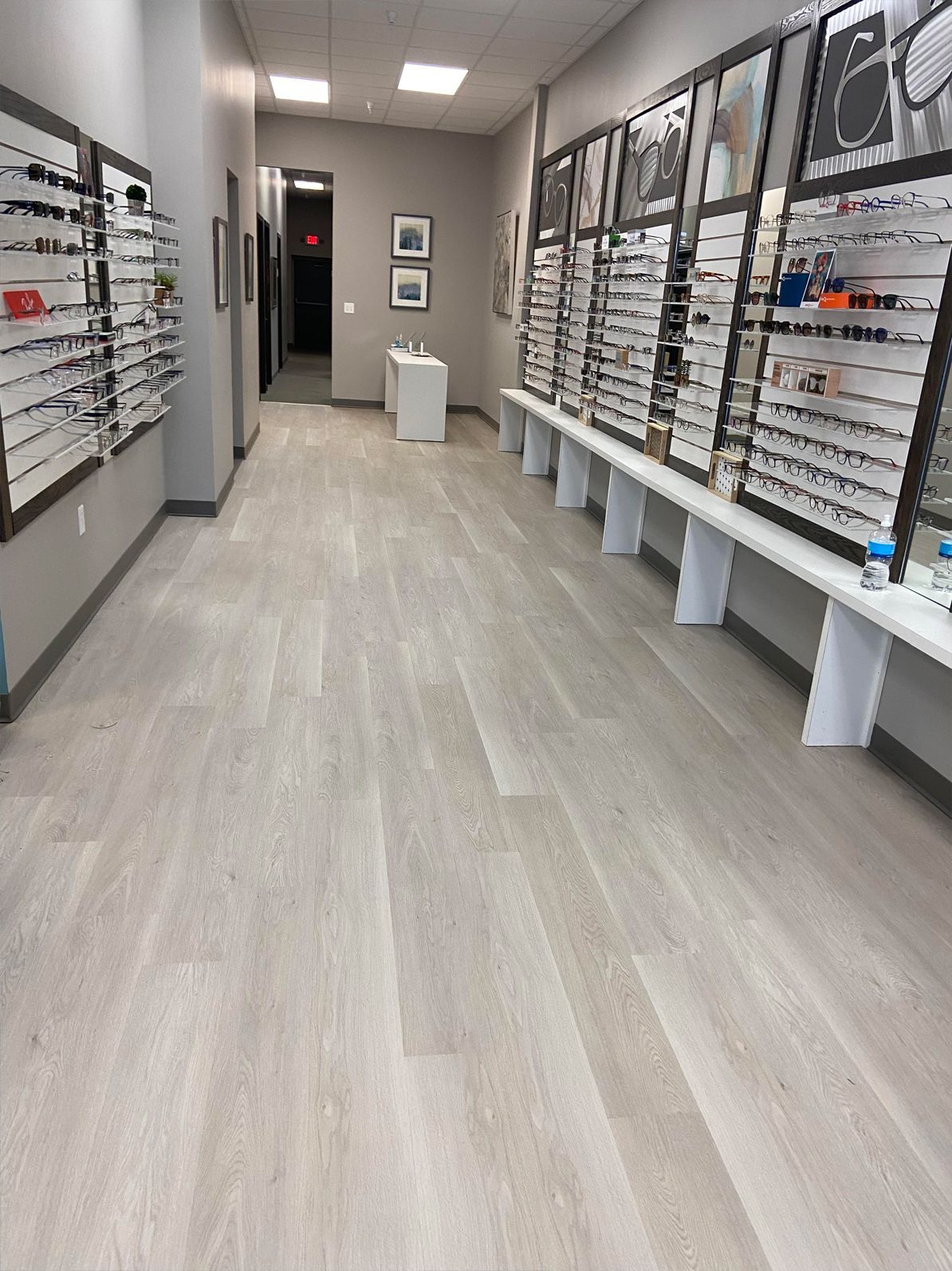 Optical store aisle with eyeglass frames displayed on both sides and a display stand at the end