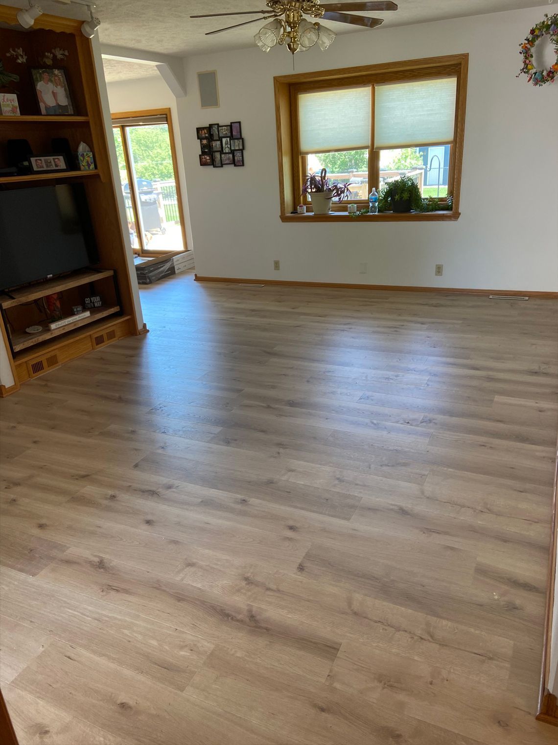 Empty living room with wood flooring, white walls, large window, and ceiling fan.
