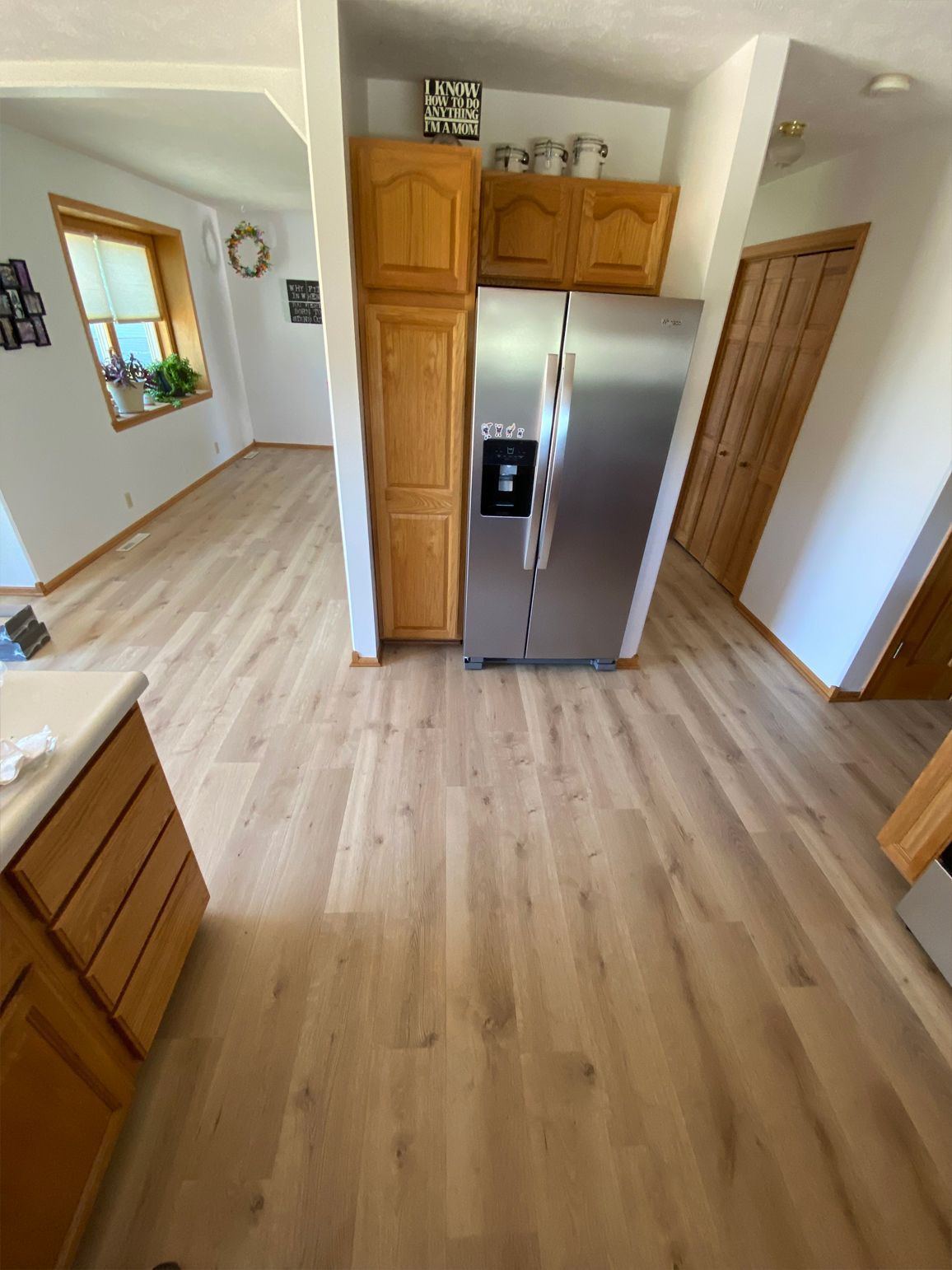 Bright kitchen with light wood floors, stainless steel refrigerator, and wooden cabinets, viewed from the center