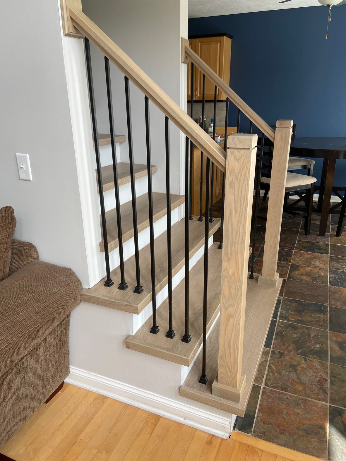 Indoor staircase with white steps, black balusters, and wood handrail beside a living room and tile floor