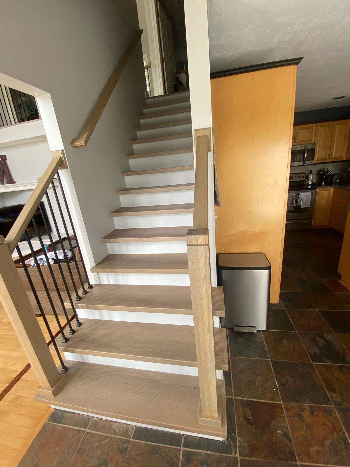 Indoor staircase with beige carpet, dark railing, and tiled floor beside a kitchen area.