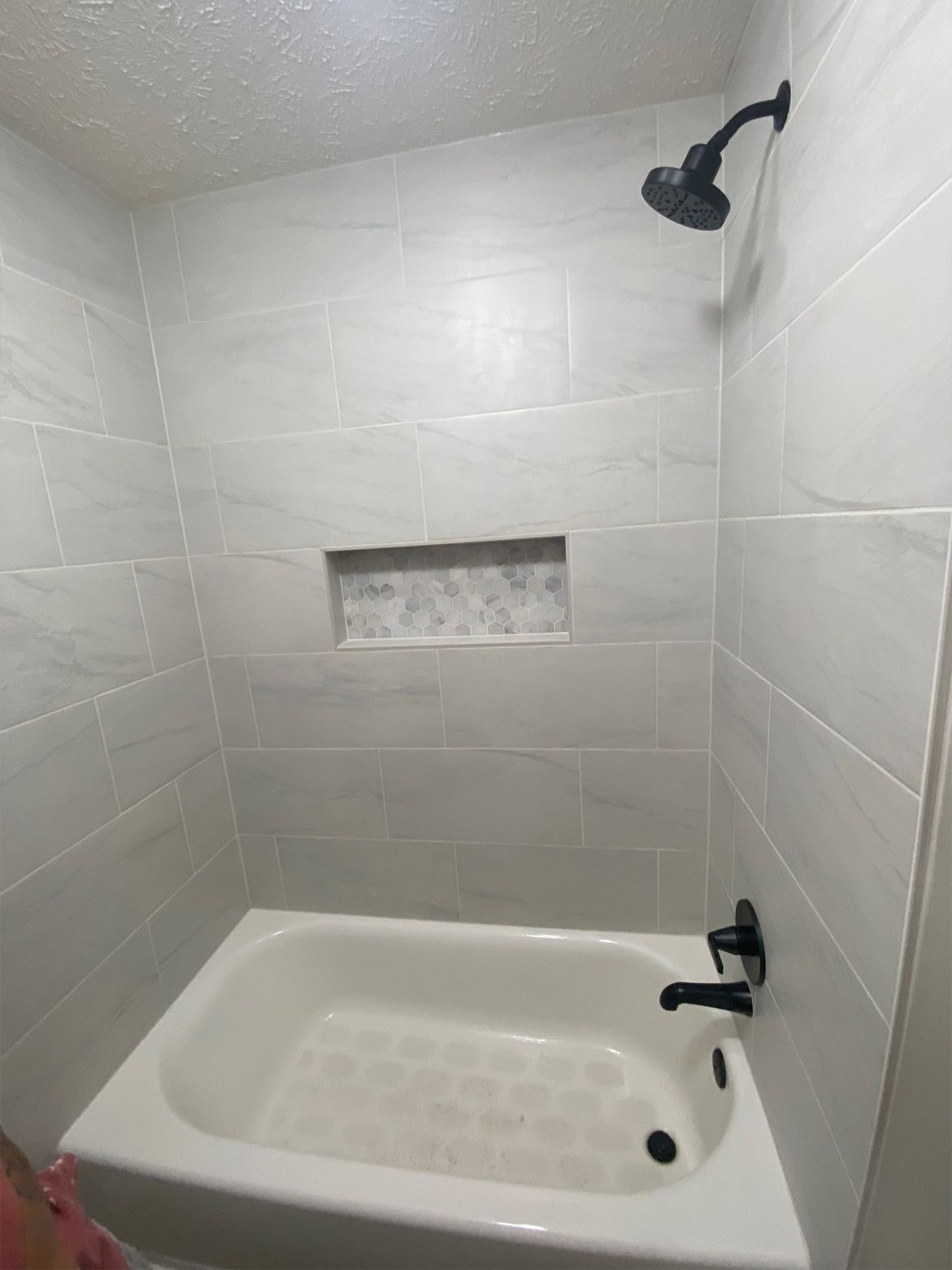 Small white-tiled shower alcove with a bathtub, black showerhead, and recessed wall niche.