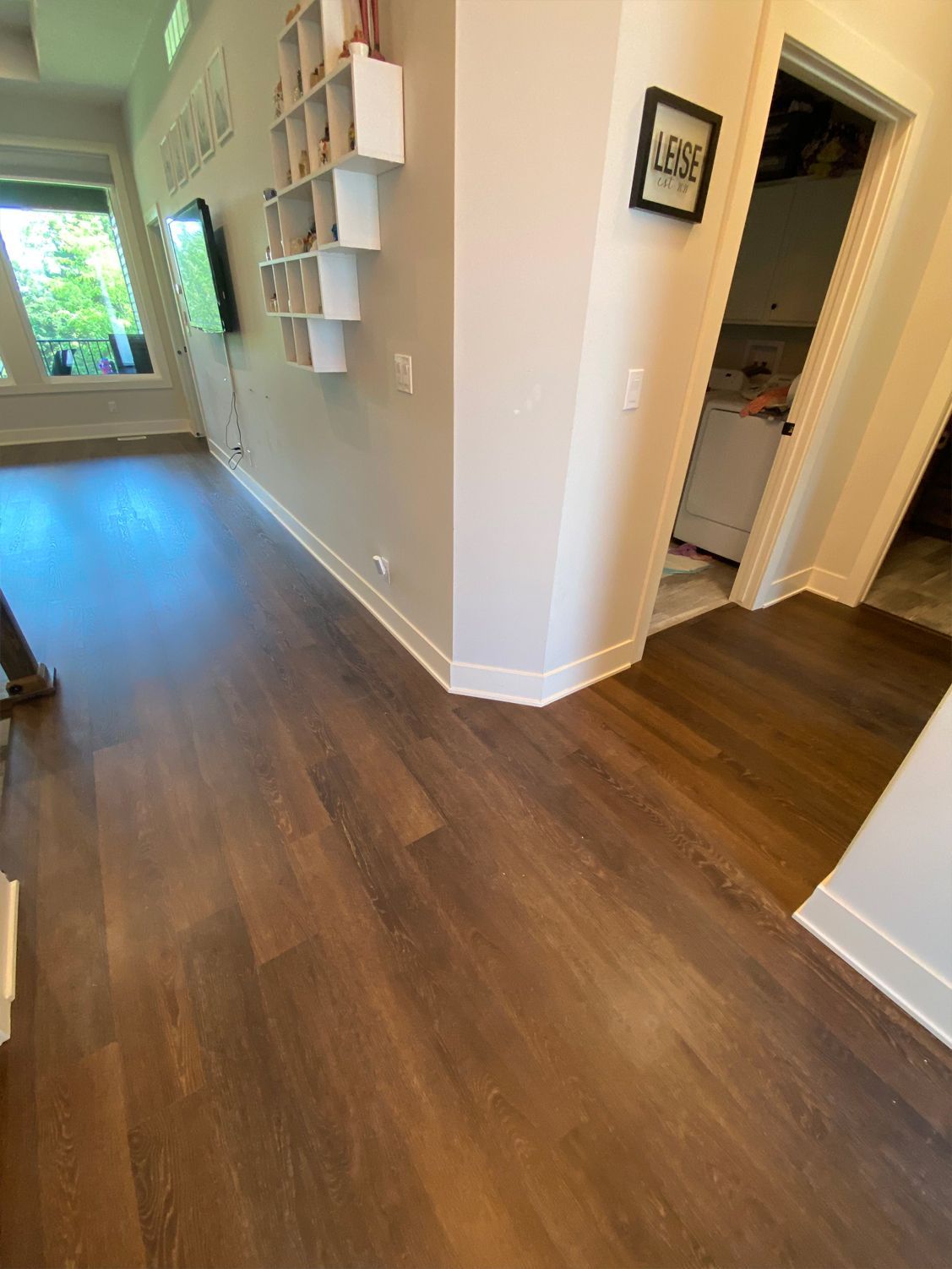 Hallway with dark wood floors, white walls, shelves, and a view into a bright room and bathroom doorway