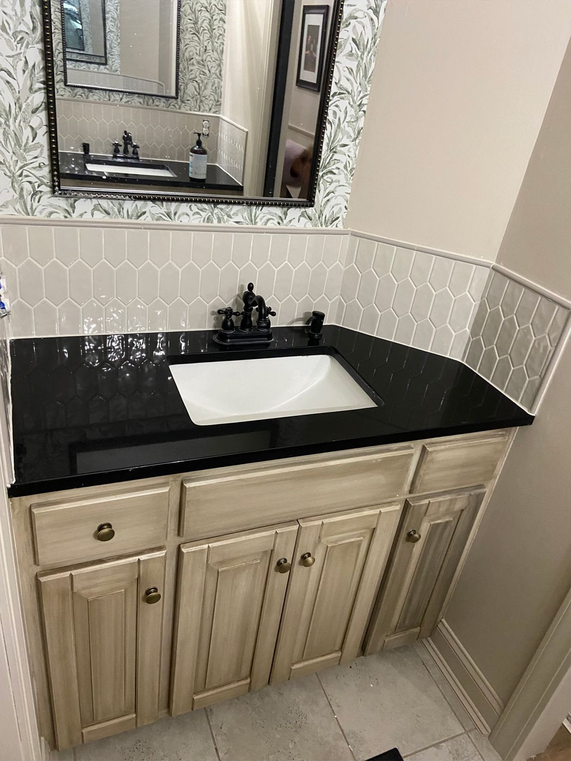Bathroom vanity with black countertop, white sink, beige cabinets, and mirror above.