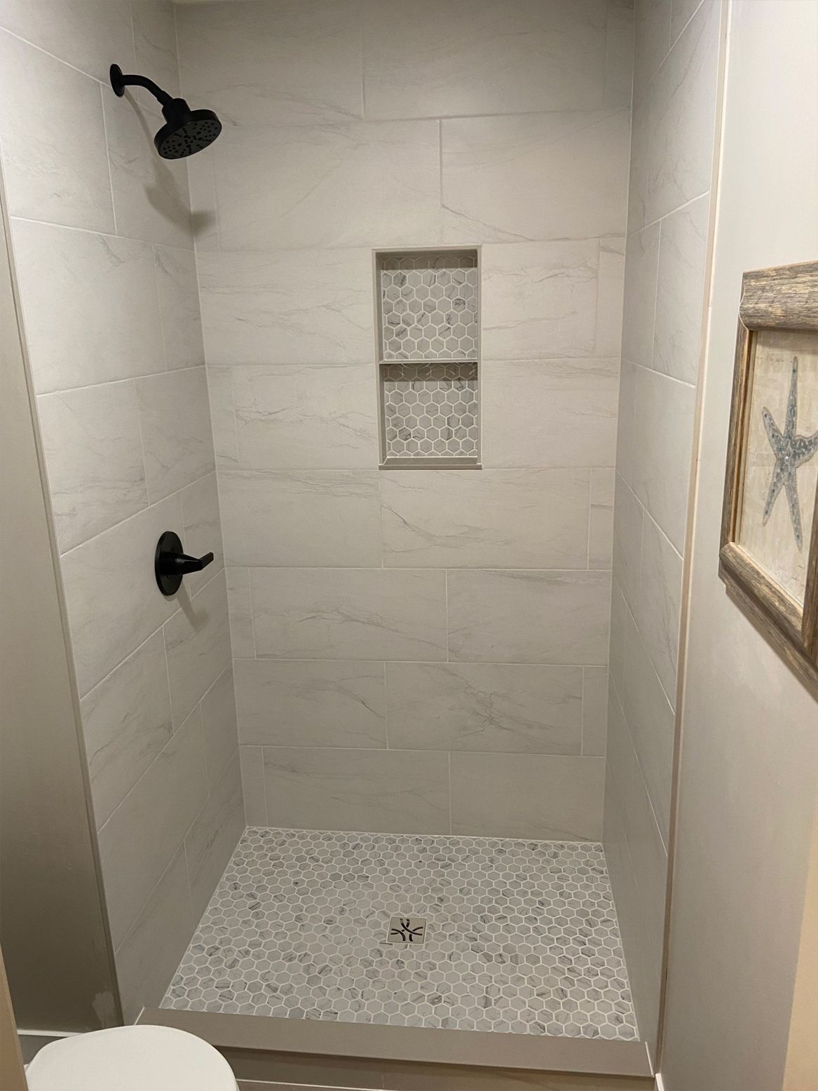 Empty tiled walk-in shower with black fixtures and pebble floor, viewed from the doorway
