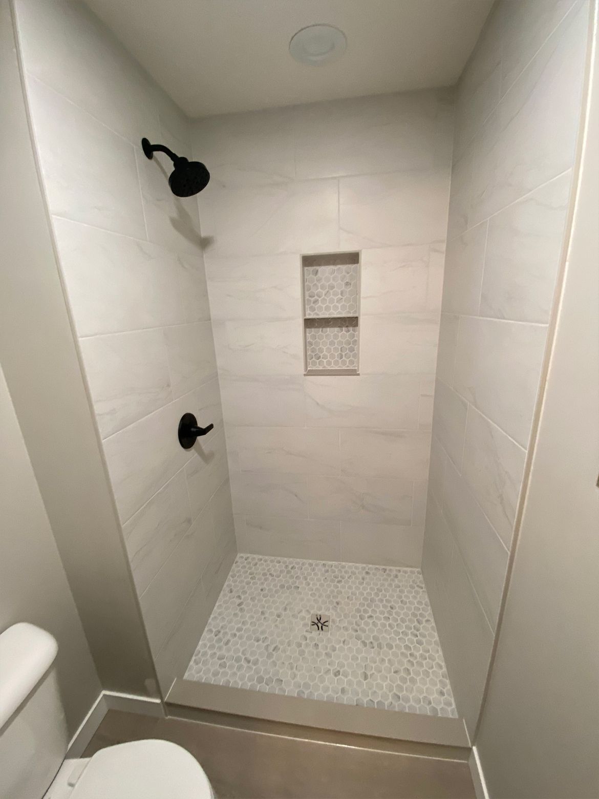 Small tiled walk-in shower with black fixtures and a built-in shelf.