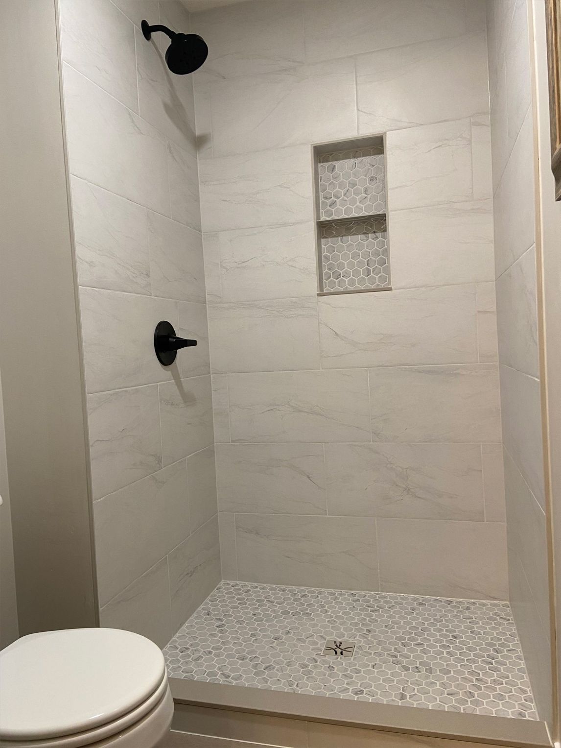 Small white tiled shower stall with black fixtures and a pebble-style shower floor.