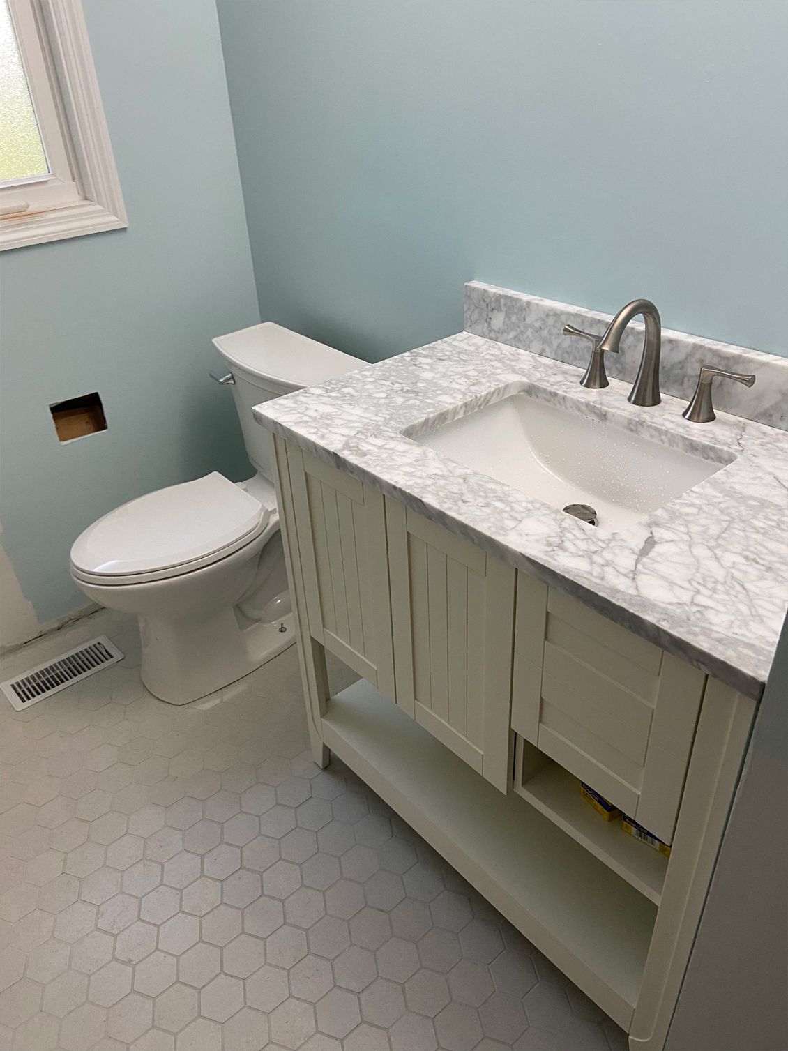 Small bathroom with white toilet, marble vanity, and light blue walls.