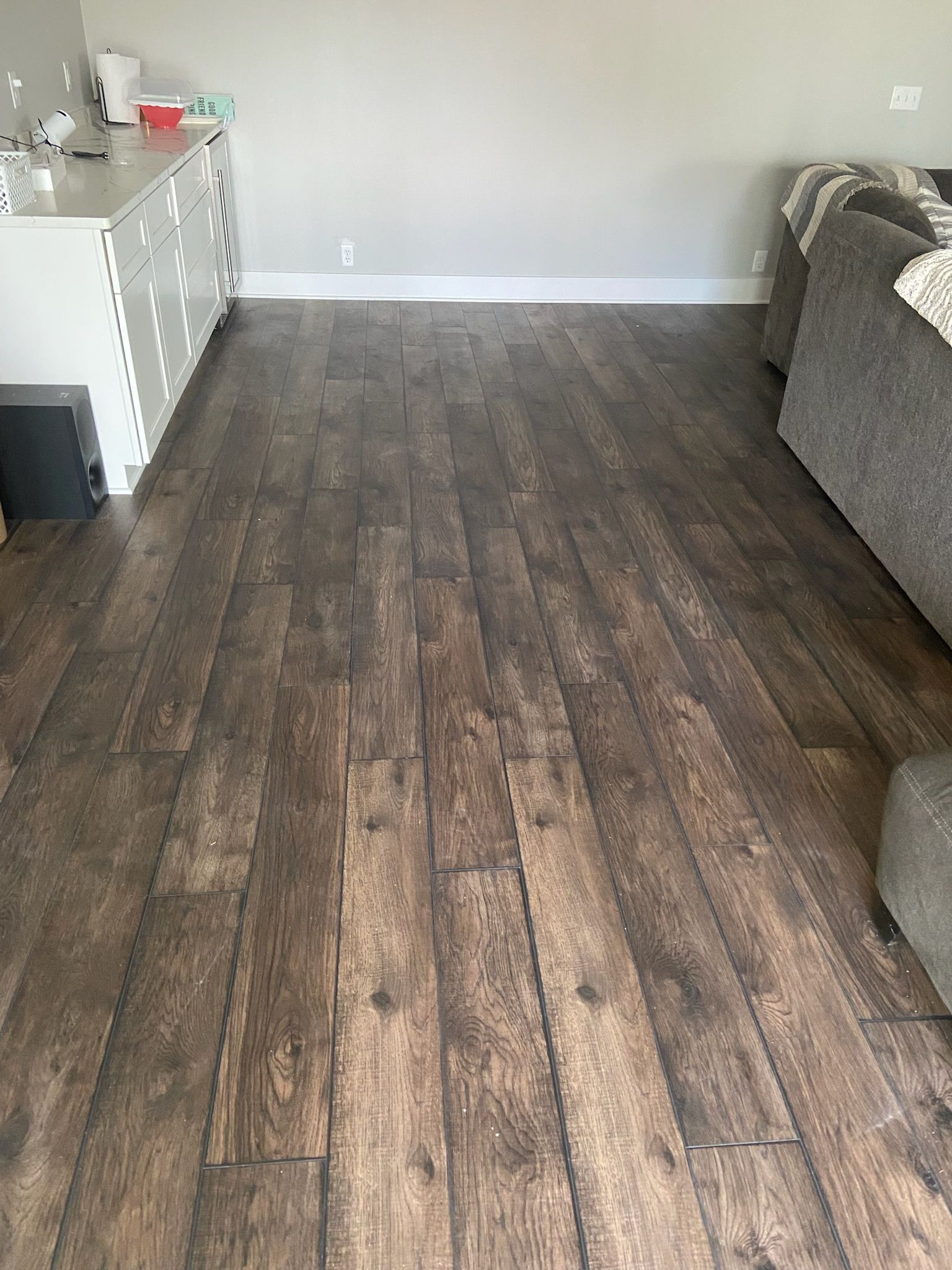 Dark wood-look flooring in a living room, with a white cabinet on the left and a gray couch on the right.