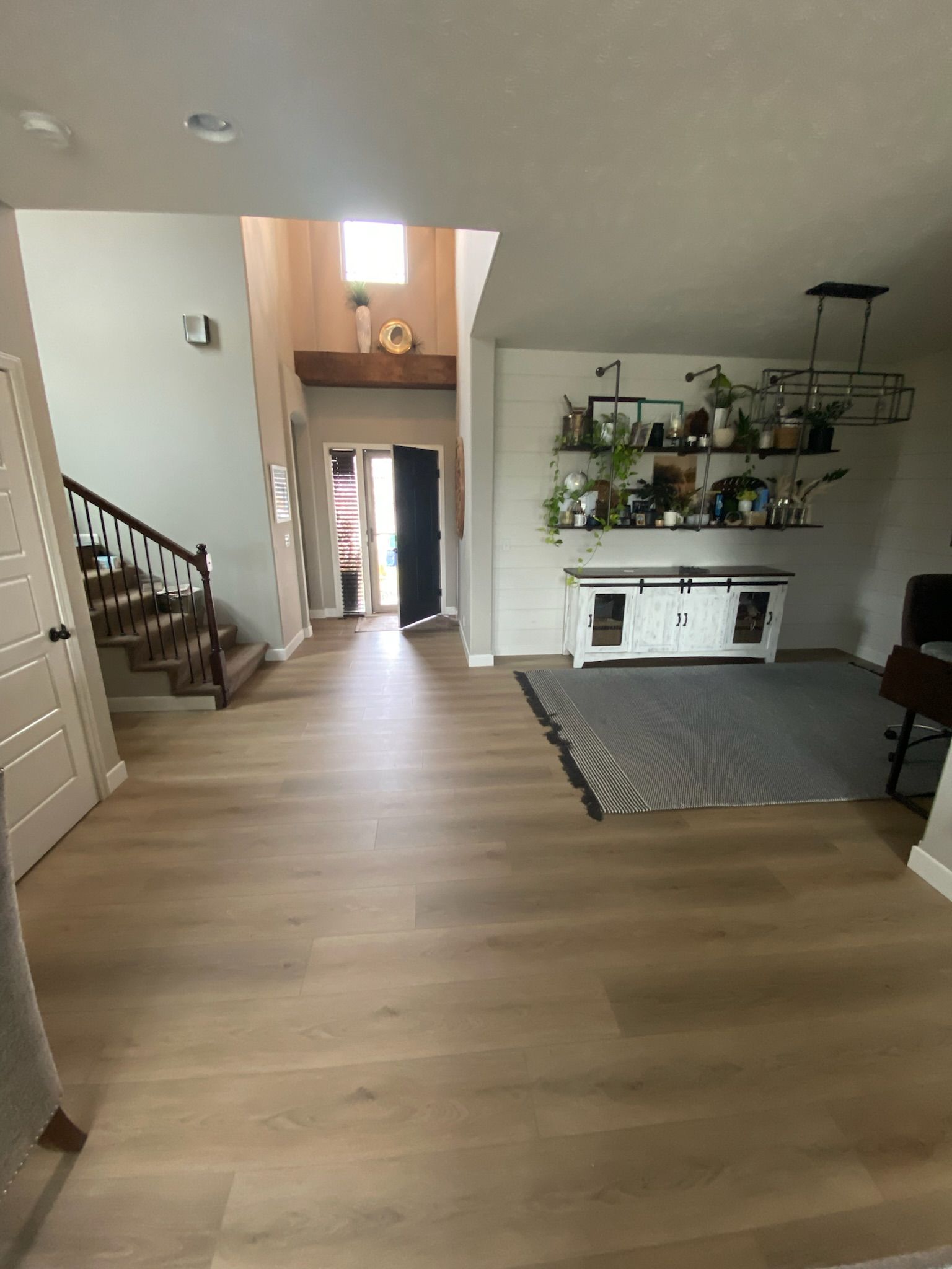 A modern entryway with wood-look flooring, staircase, plants on shelving, and a cabinet.