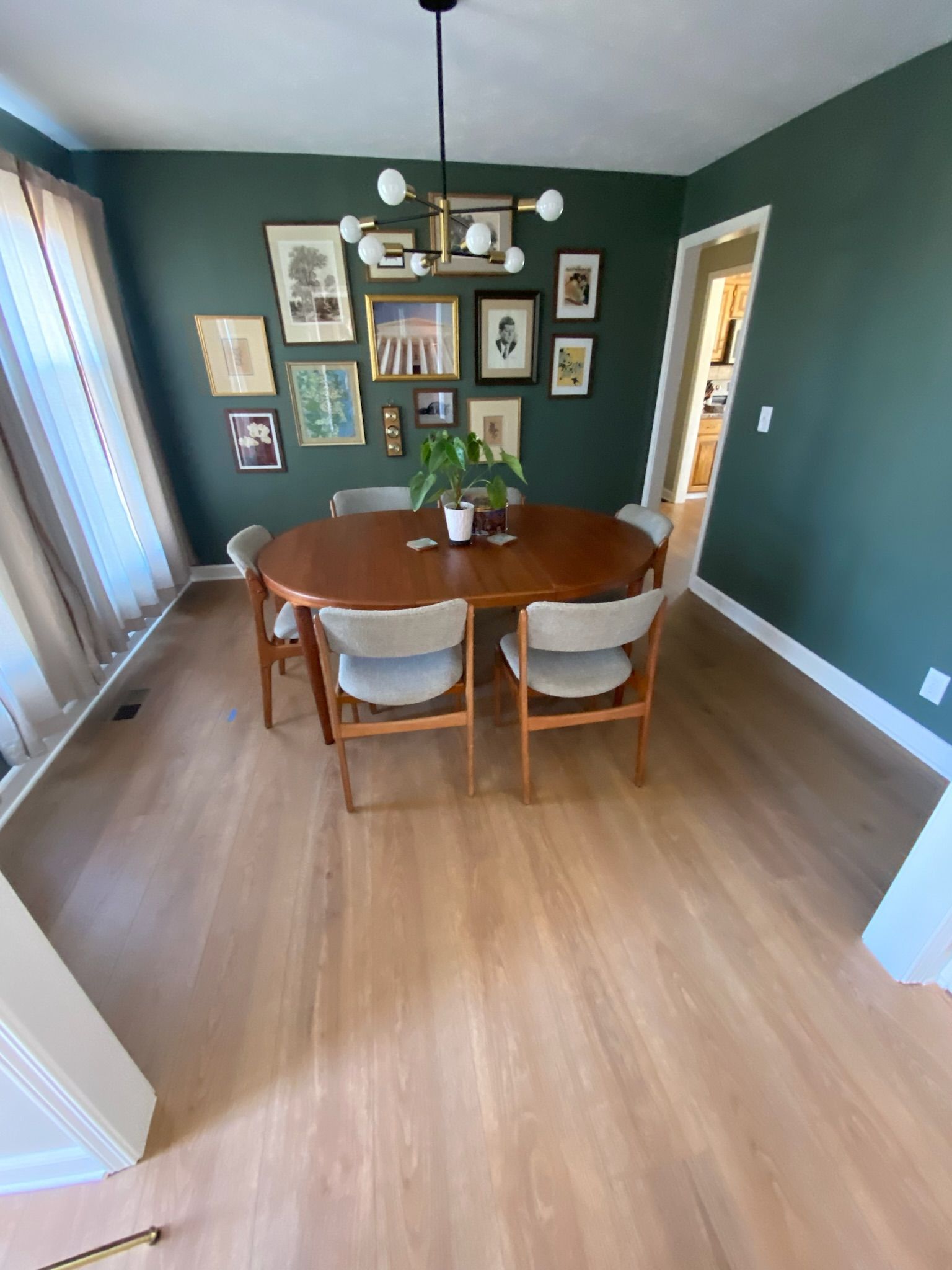 Dining room with wooden table and chairs, gallery wall, green walls, and light wood flooring.
