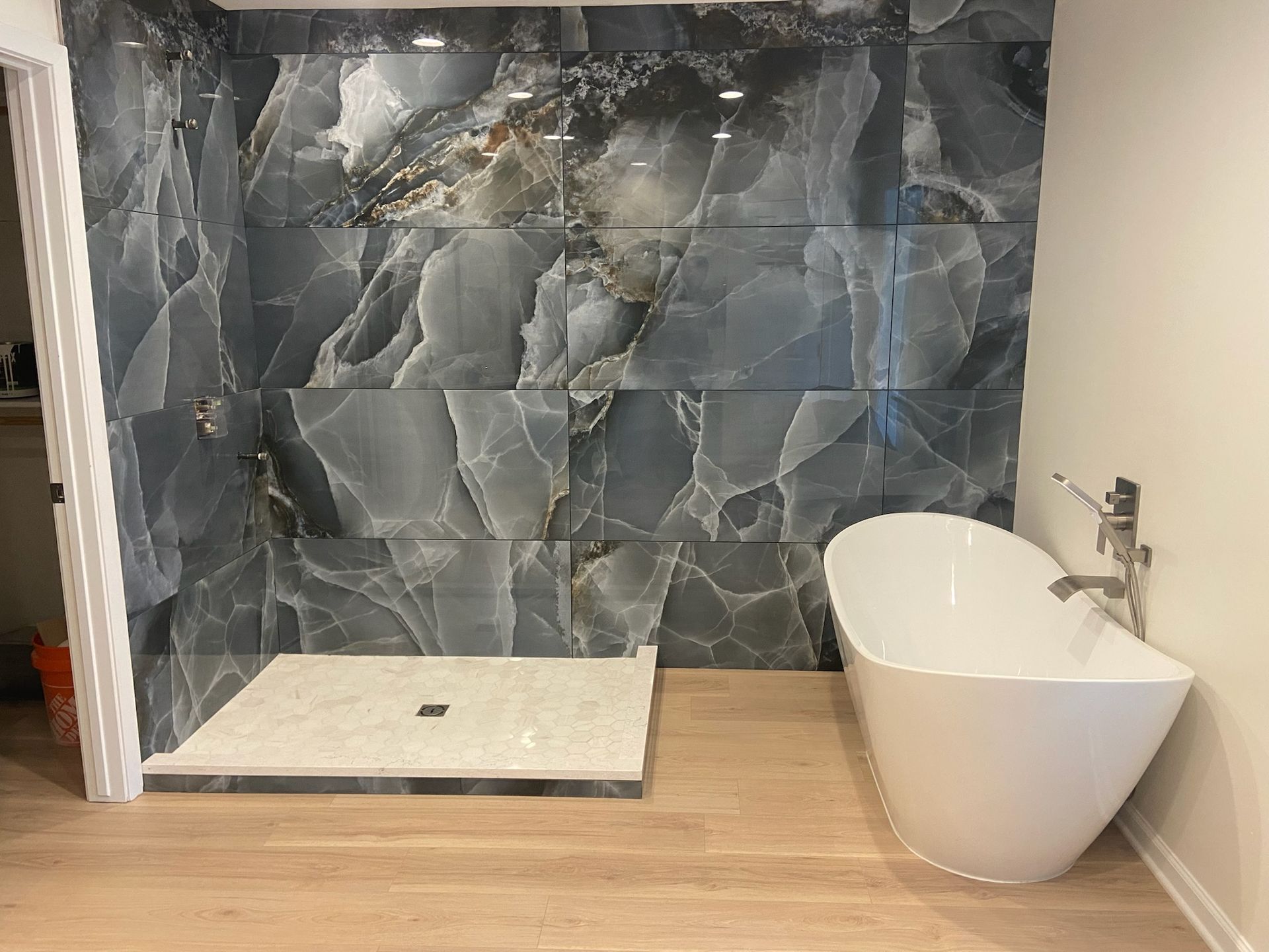 Bathroom with marble-like blue tile shower, white soaking tub, and wood-look flooring.