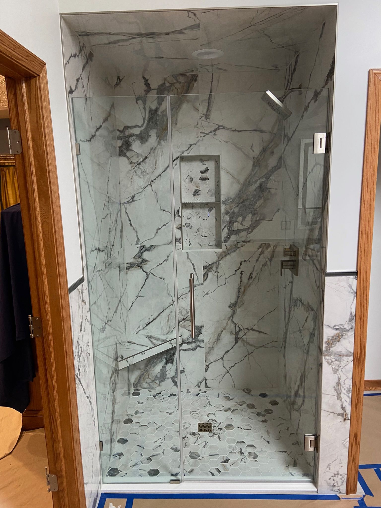 A newly renovated shower with marble-look tiles, glass door, and silver fixtures.