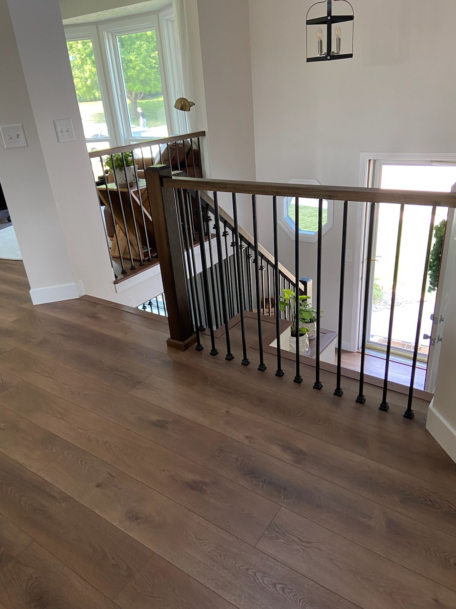 Interior view of a staircase with wood flooring, dark metal railing, and a view of the front door.