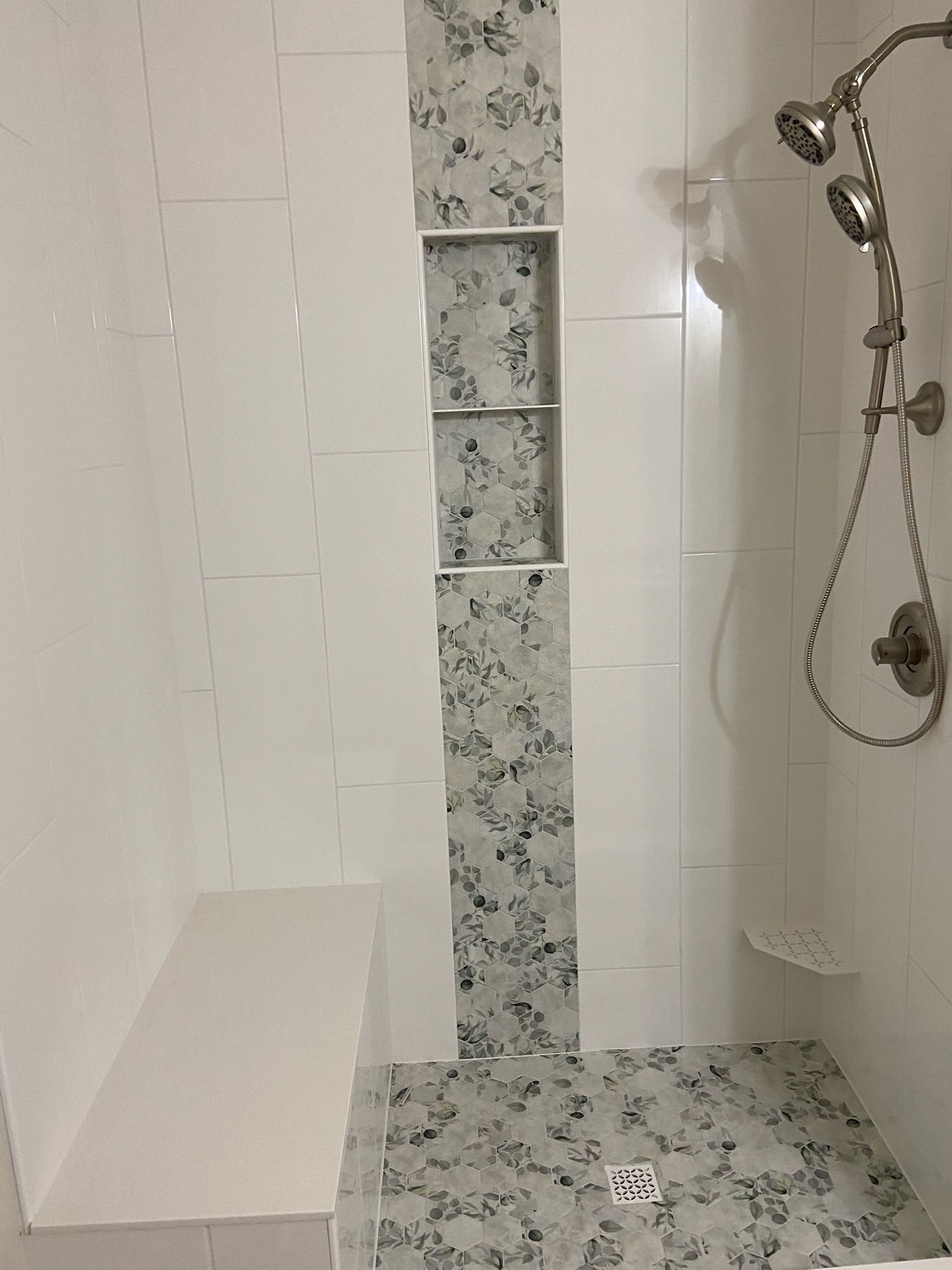 White tiled shower with decorative central strip and built-in bench. Silver showerhead on right.