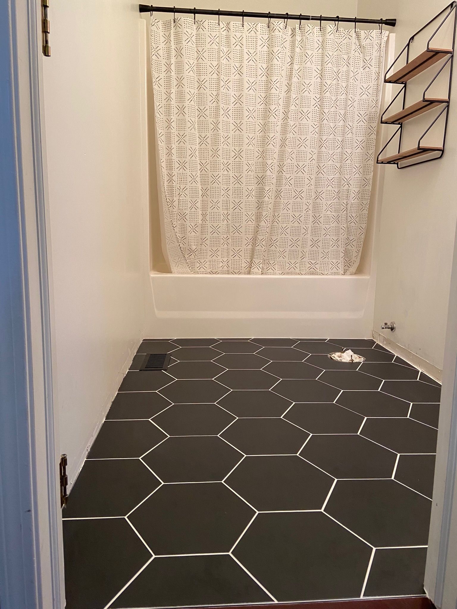 Bathroom with dark hexagon tile floor, white walls, and a patterned shower curtain.