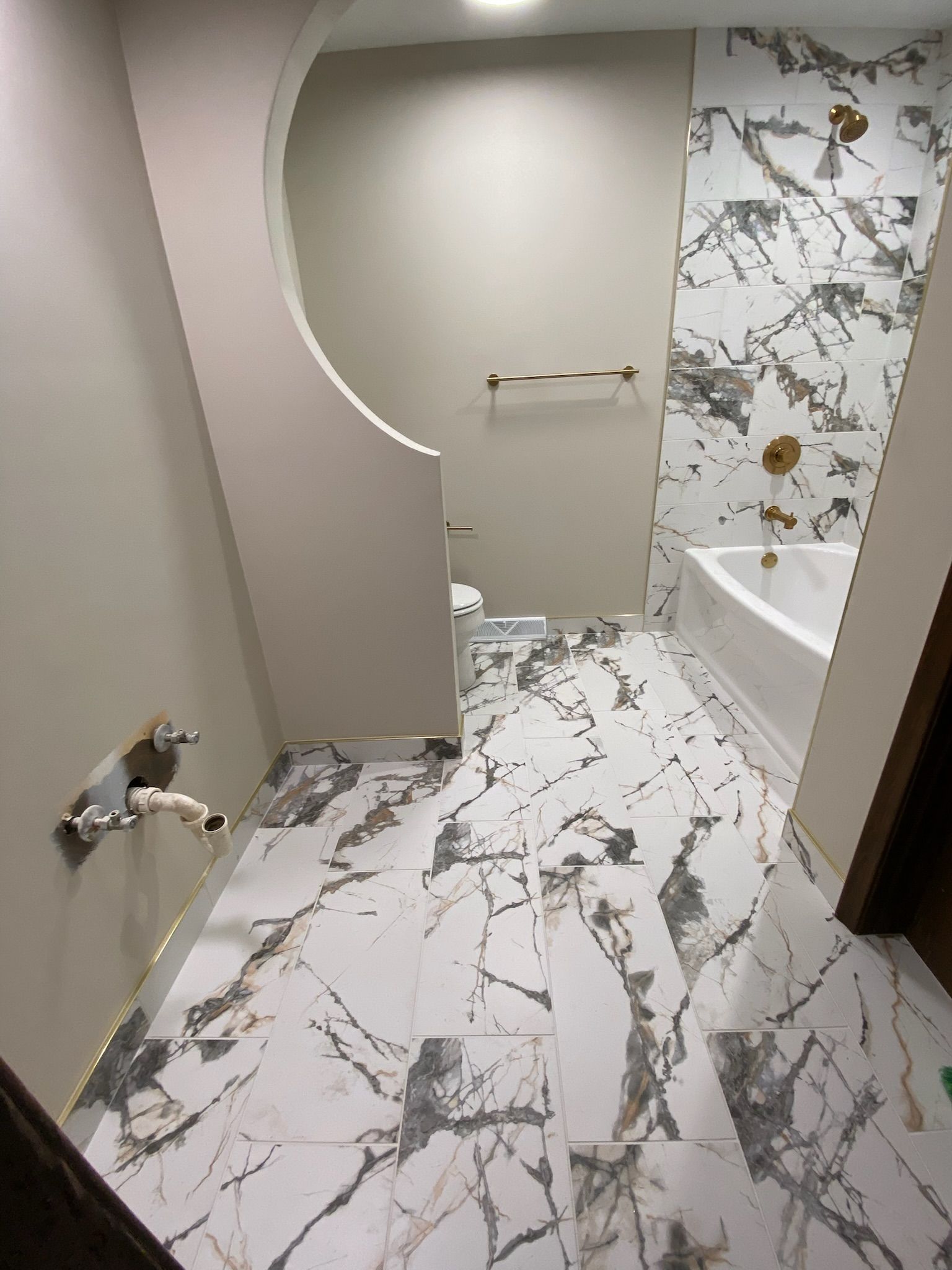 Bathroom with marble tile floor and wall. White tub, gold fixtures.