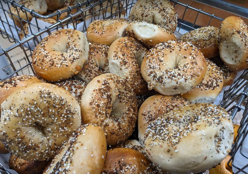 A bunch of bagels in a basket with sesame seeds on them