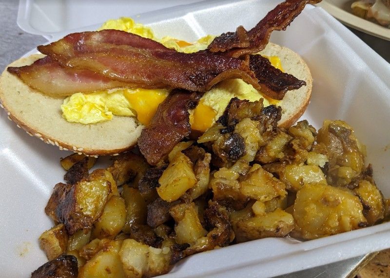 A sandwich with bacon eggs and potatoes in a styrofoam container