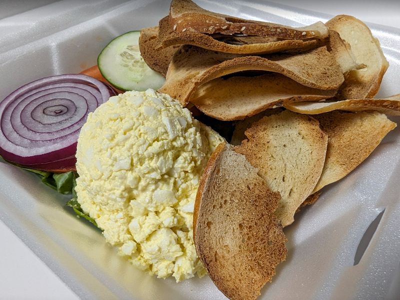 A styrofoam container filled with a salad and chips.