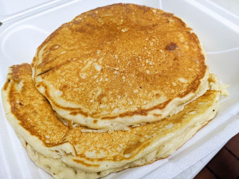 Two pancakes are stacked on top of each other in a styrofoam container.