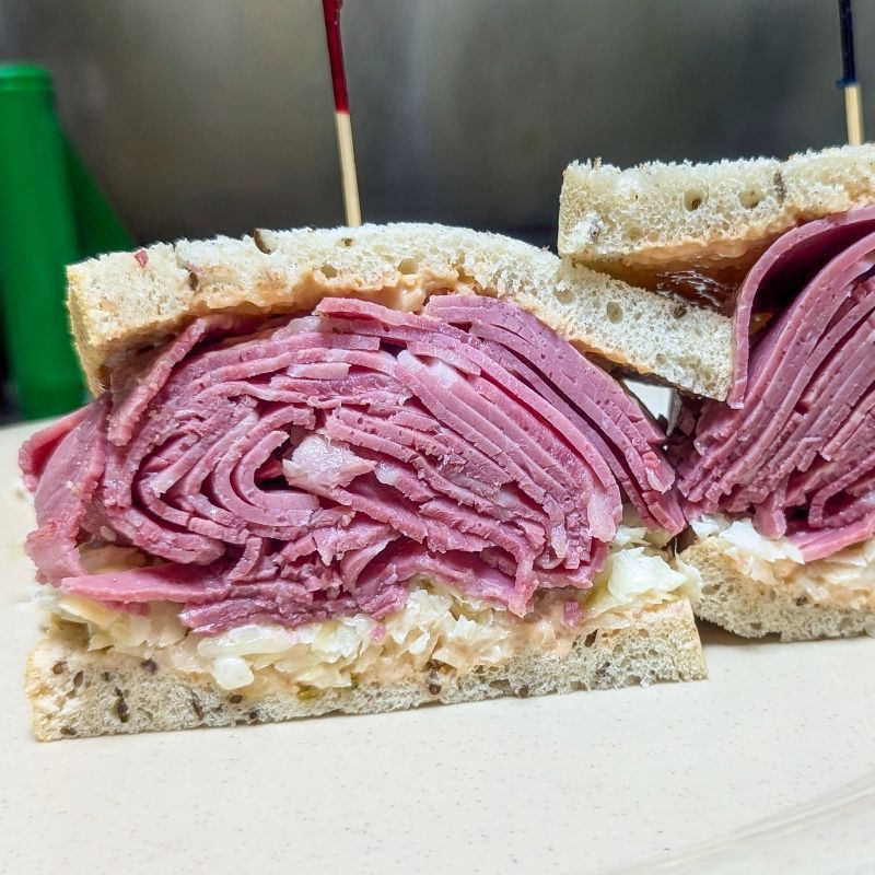 A corned beef sandwich is cut in half on a wooden cutting board.
