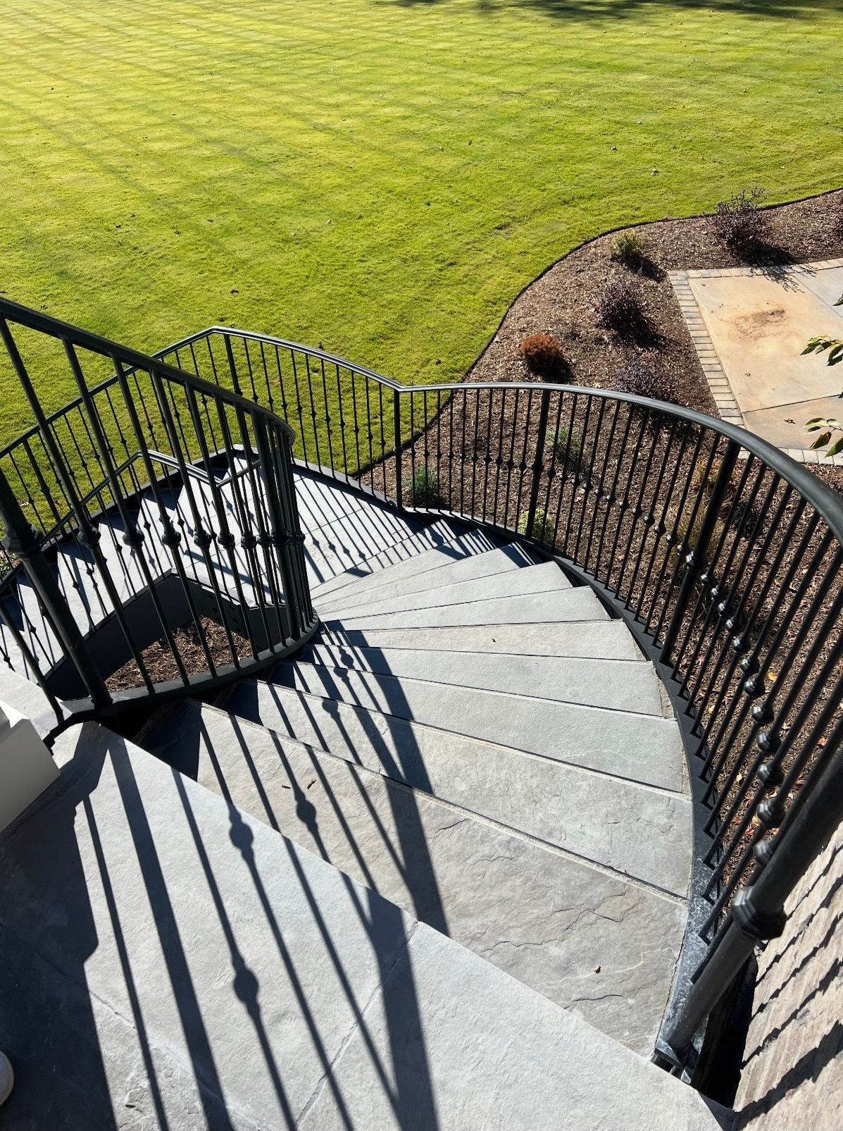A spiral staircase with a wrought iron railing leading up to a lush green field.