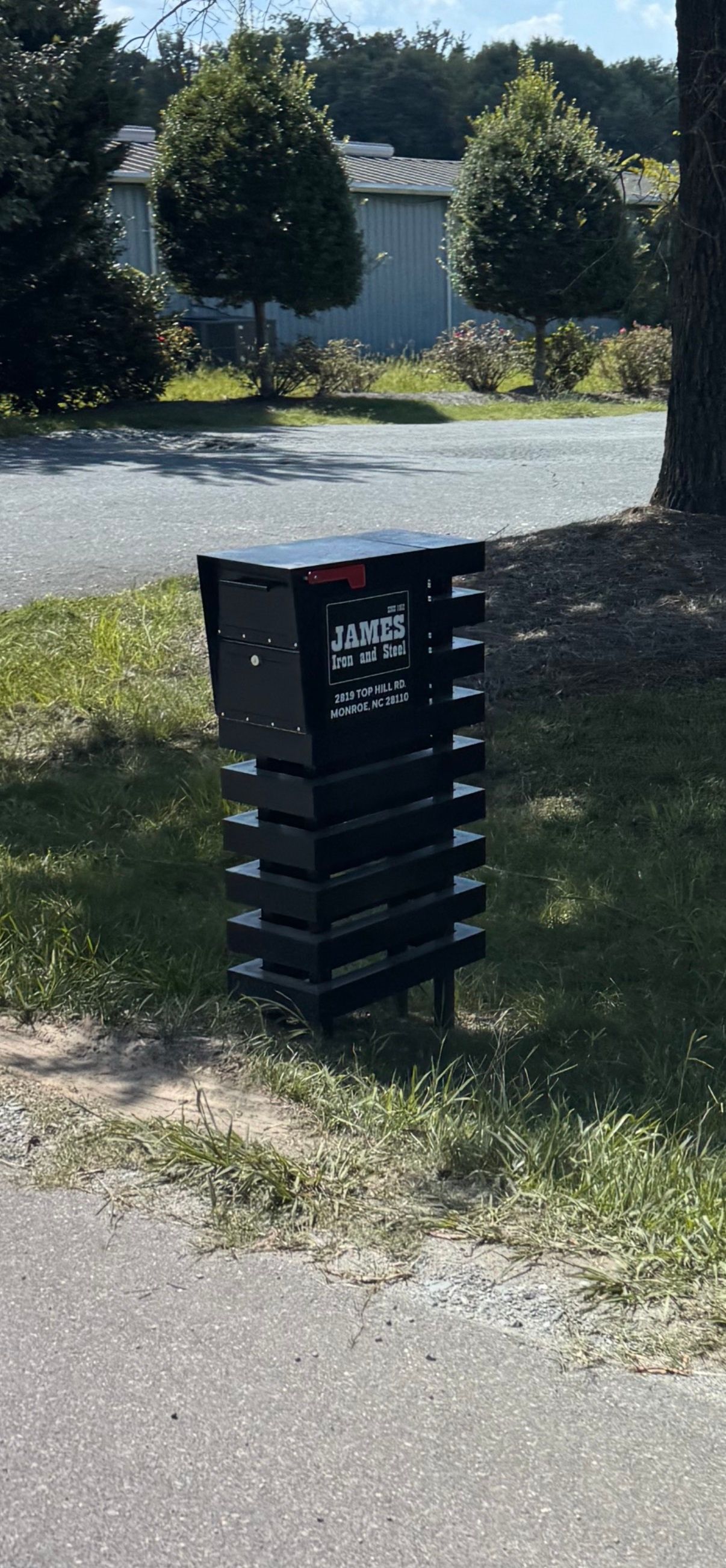A black mailbox is sitting in the grass next to a road.