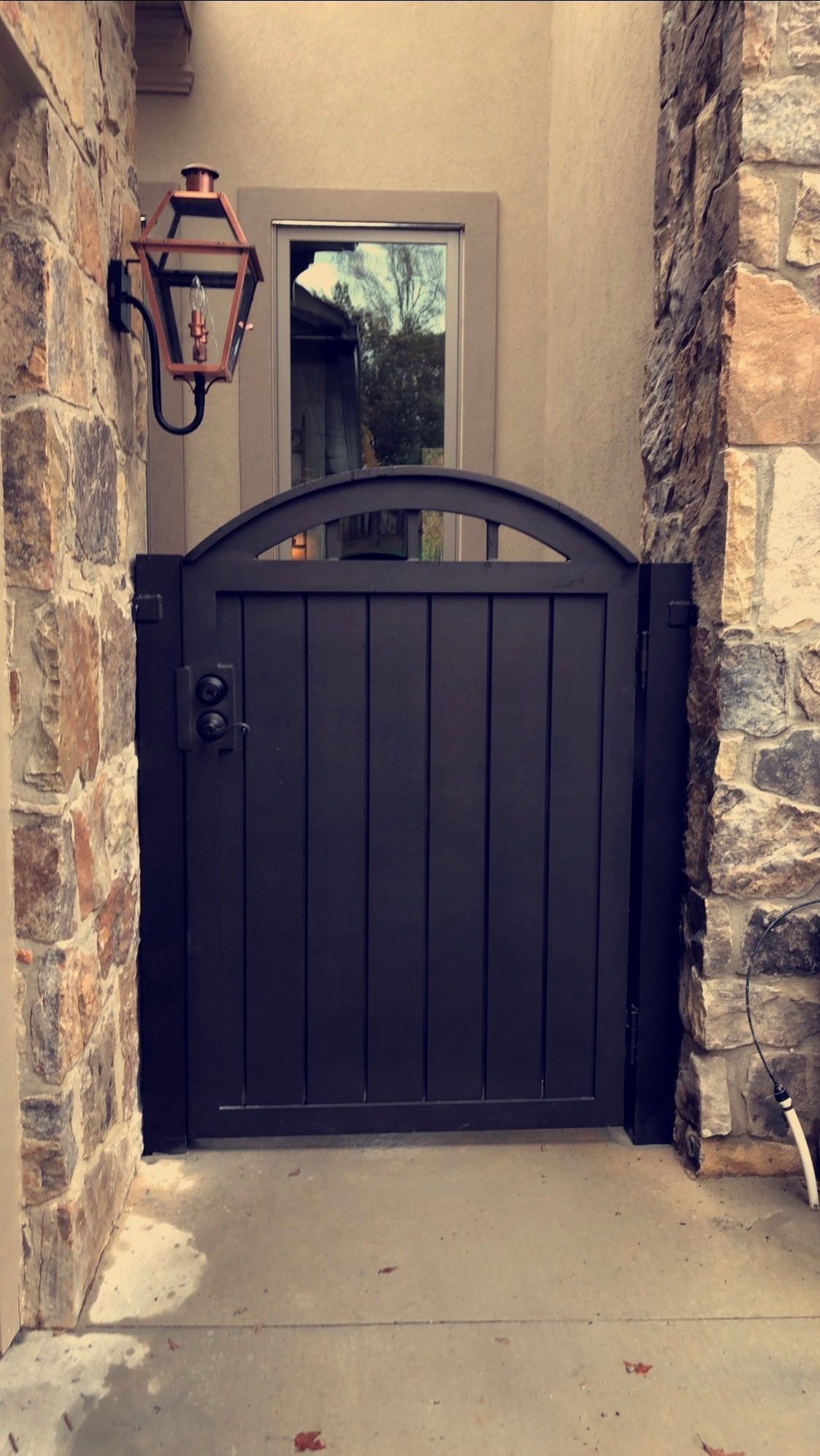 A black gate is sitting next to a stone wall.
