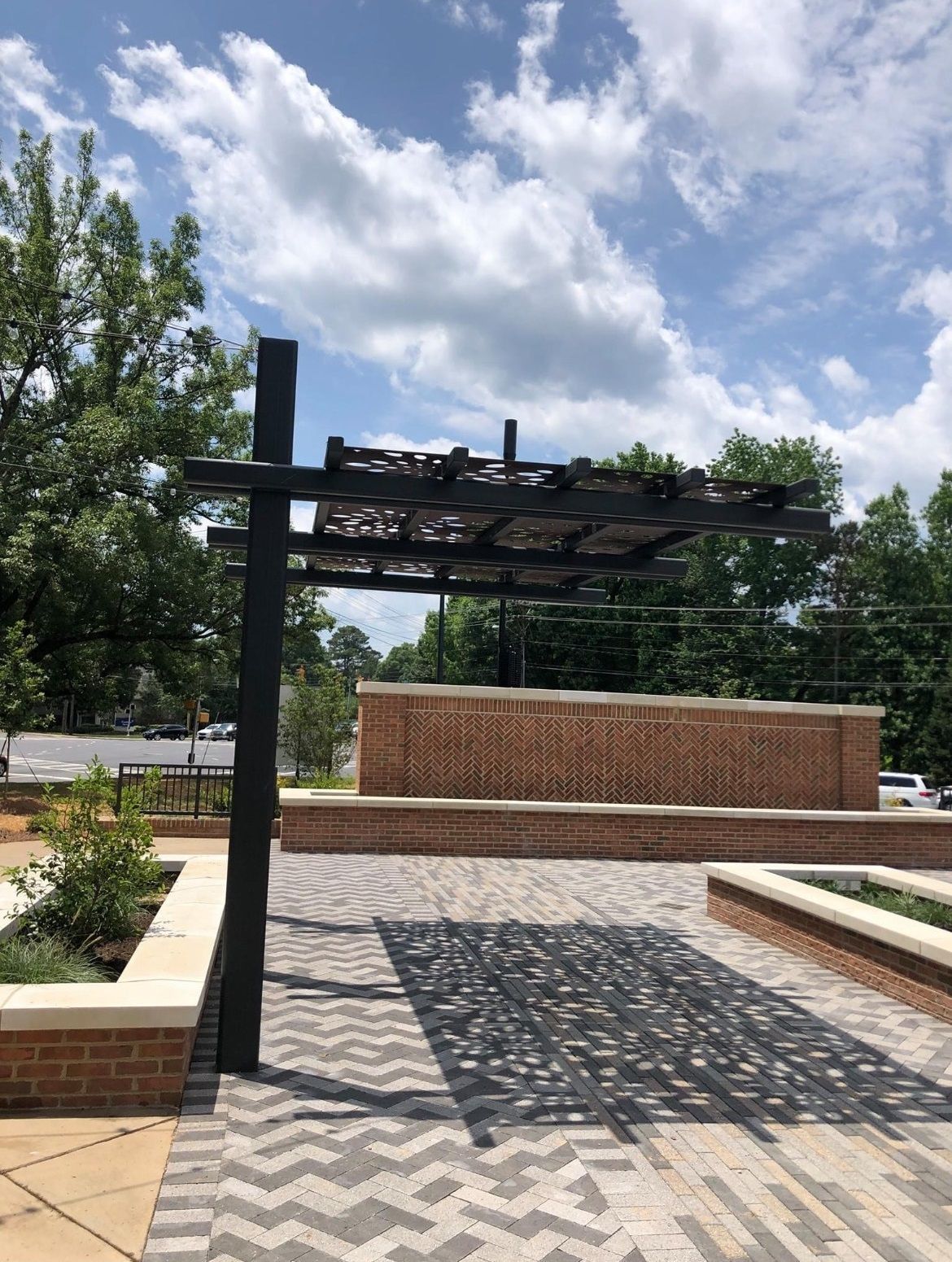 A pergola is sitting in the middle of a brick courtyard.