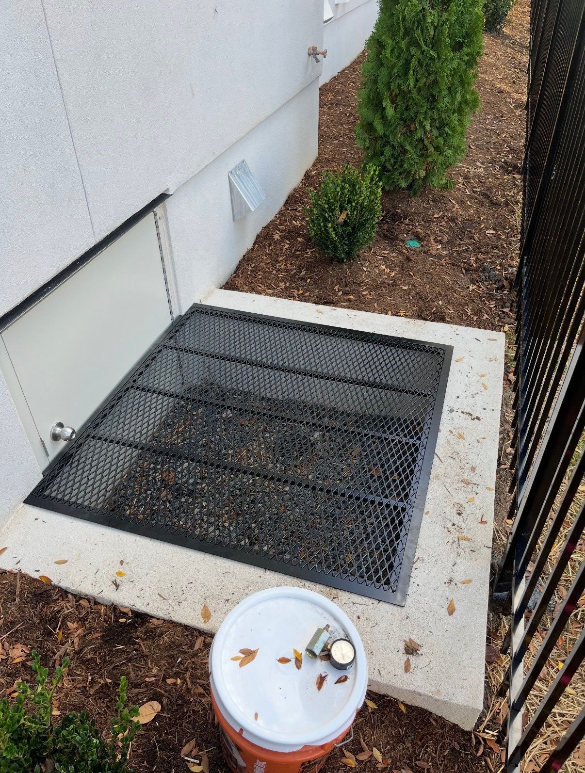 A bucket of paint is sitting on the ground next to a window.