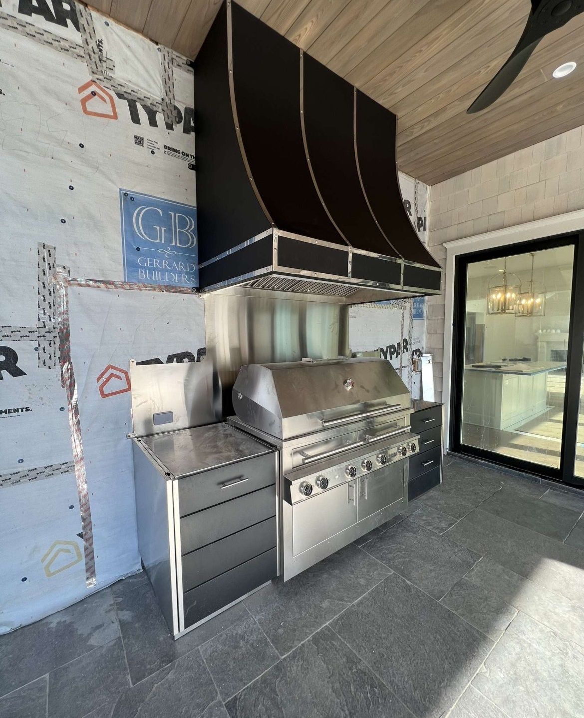 A stainless steel grill with a black hood is sitting under a ceiling fan.