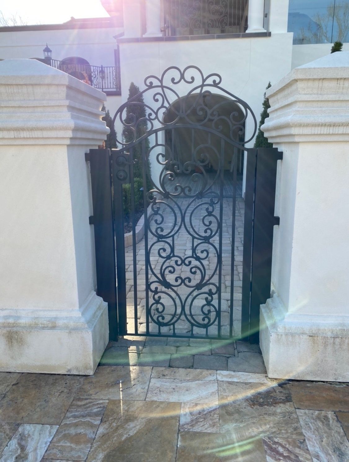 A wrought iron gate is between two white pillars.