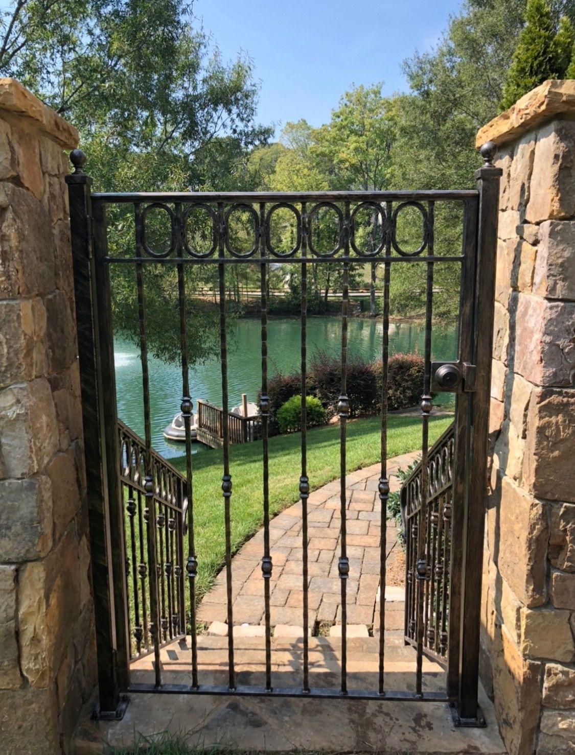 A wrought iron gate leads to a stone walkway leading to a lake.