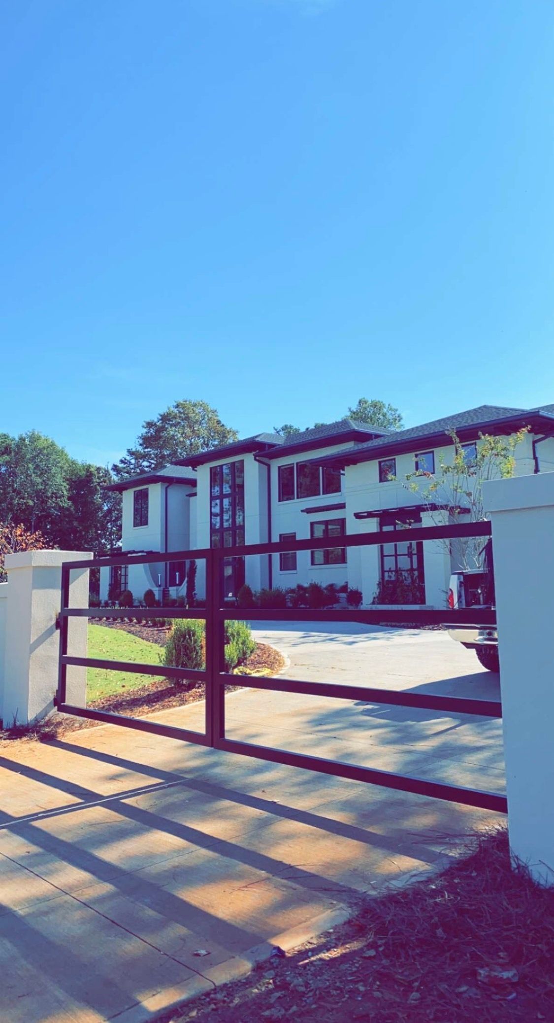 A large white house is behind a wooden gate on a sunny day.