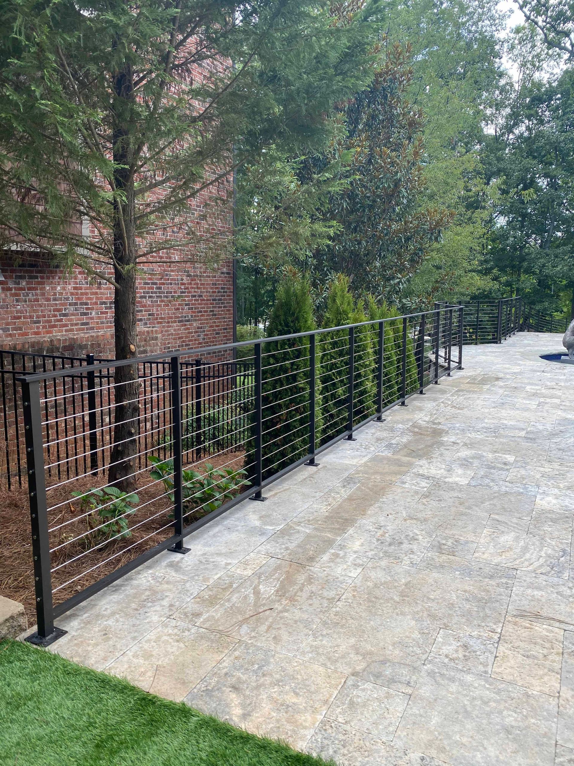 A black metal fence surrounds a driveway in front of a brick house.