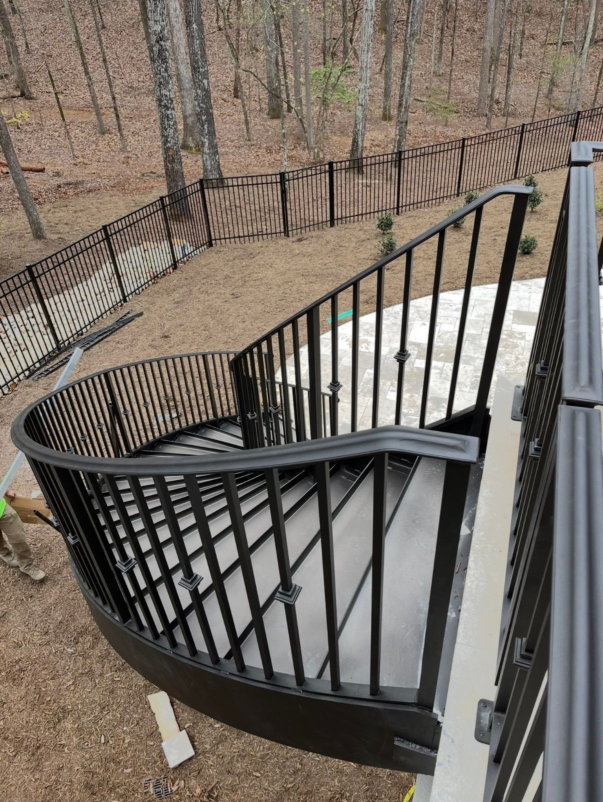 A spiral staircase with a black railing and a fence in the background.