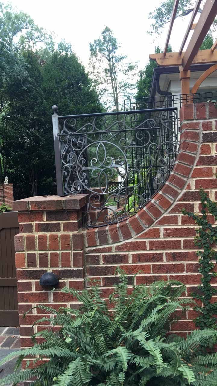 A brick wall with a wrought iron railing and a pergola in the background.