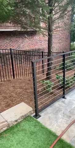 A black wire fence is surrounding a lush green yard.