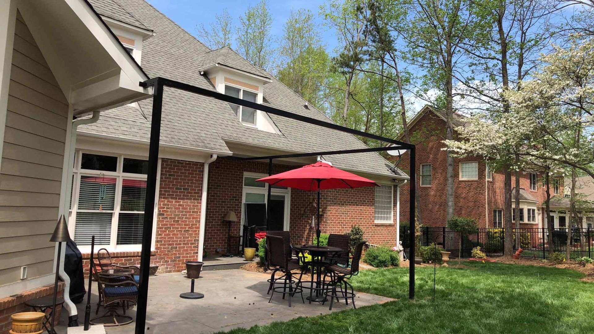 A patio with a table and chairs under an umbrella in front of a brick house.