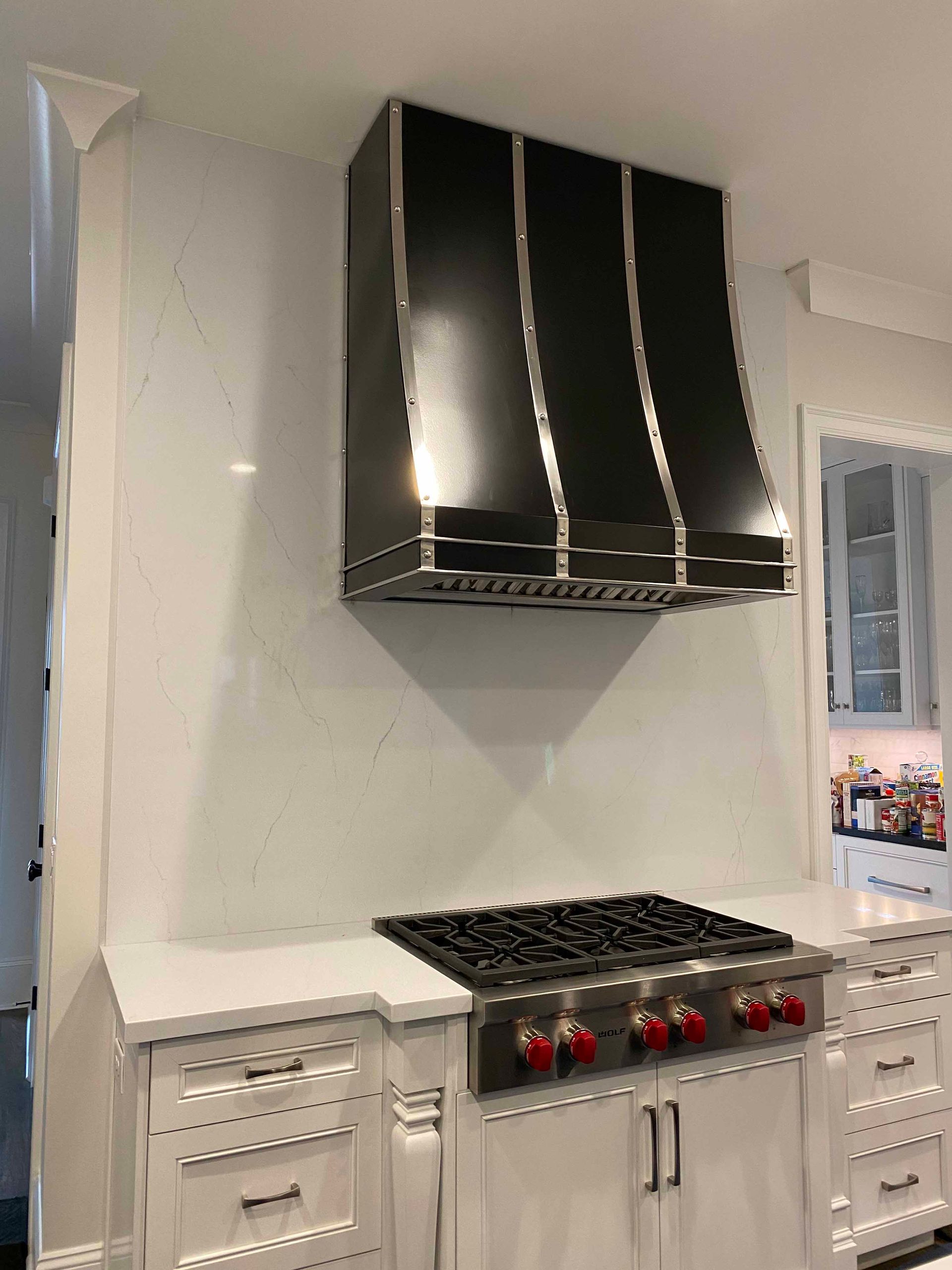 A kitchen with a stove top oven and a black hood.