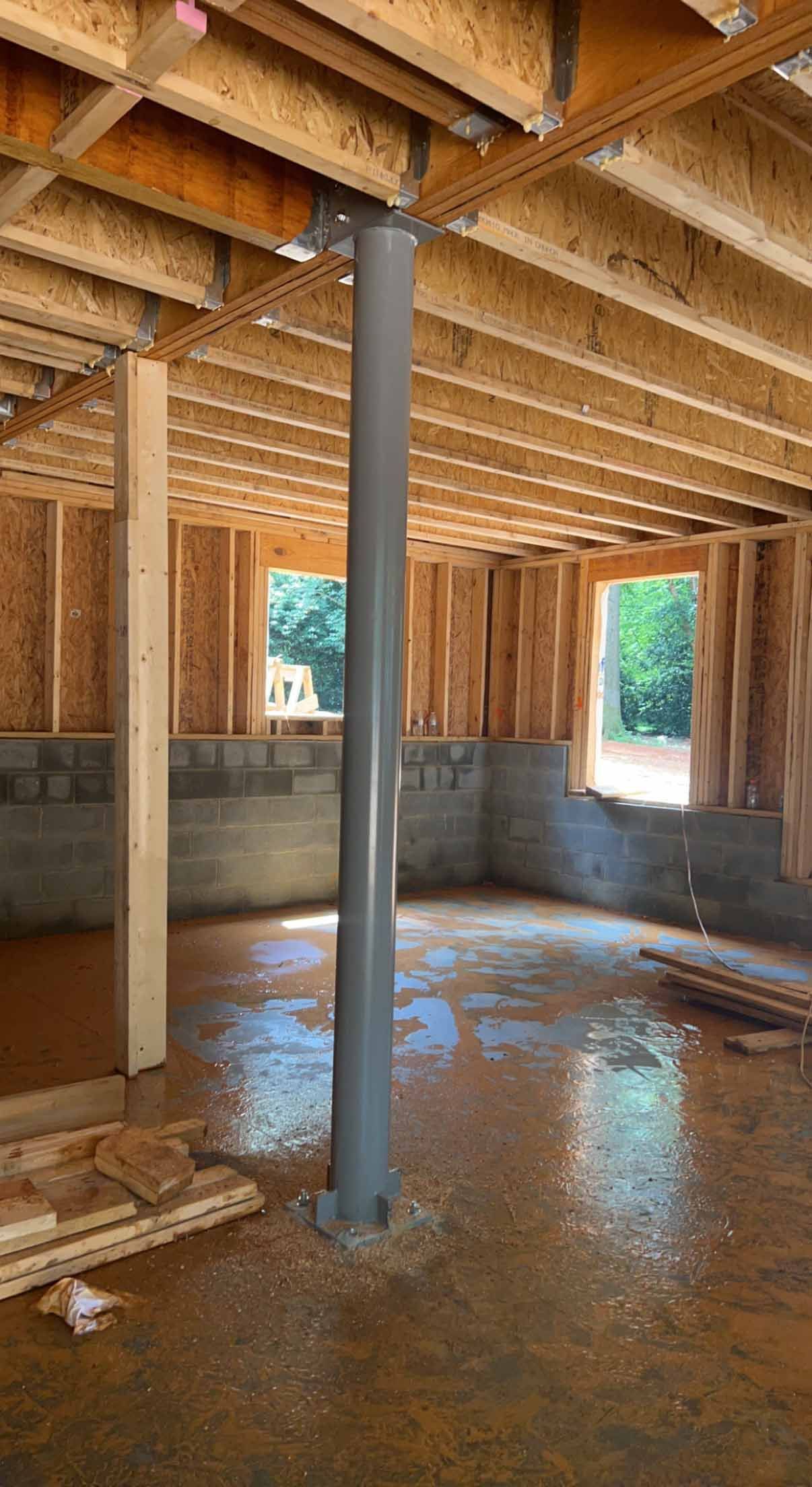 A basement under construction with a gray pipe in the middle of the room.